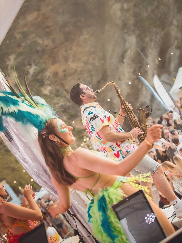 Paul Haywood performing live saxophone at the Ibiza Classics night, Lusty Glaze Beach, Newquay. A full-stage show featuring DJ, percussion, and samba dancers, bringing an Ibiza-style beach party atmosphere to a packed crowd.